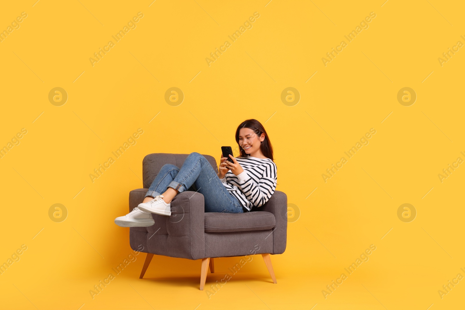 Photo of Smiling woman with smartphone sitting in armchair on yellow background