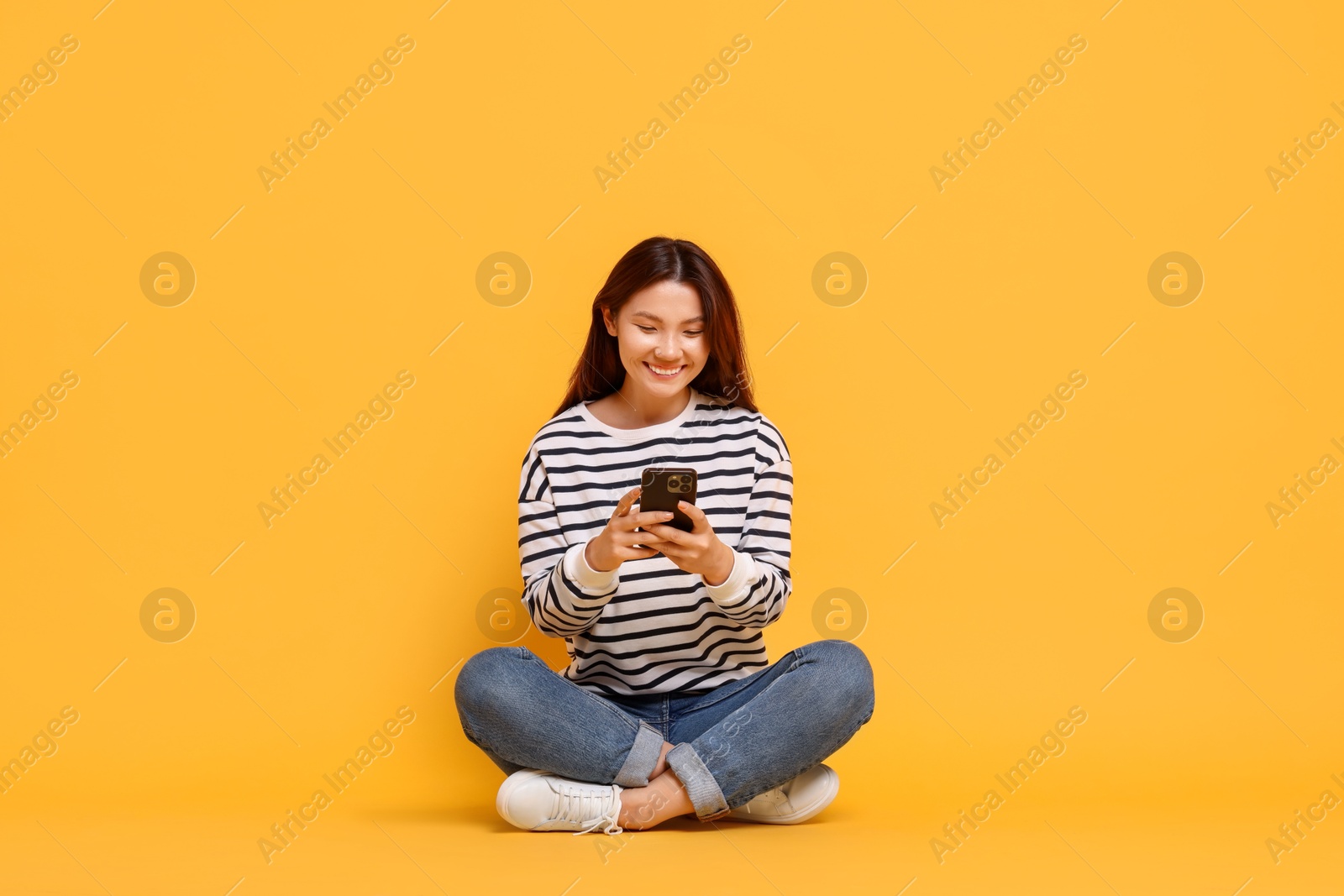 Photo of Smiling young woman using smartphone on yellow background