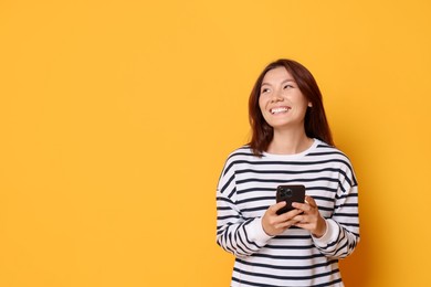 Photo of Smiling young woman with smartphone on yellow background. Space for text