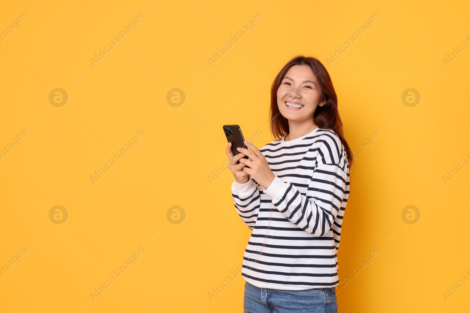 Photo of Smiling young woman with smartphone on yellow background. Space for text