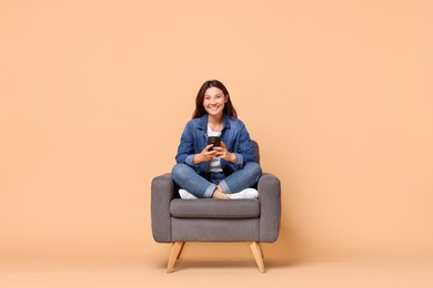 Photo of Smiling woman with smartphone sitting in armchair on beige background