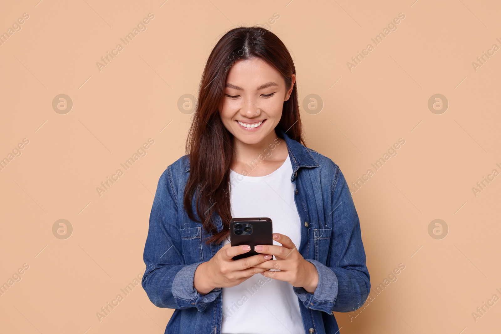 Photo of Smiling woman using smartphone on beige background