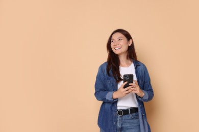 Photo of Smiling woman with smartphone on beige background. Space for text