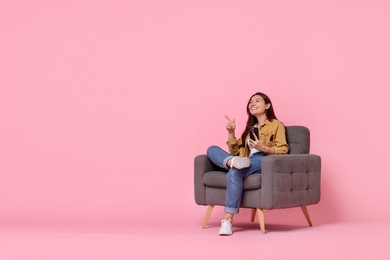 Photo of Smiling woman with smartphone sitting in armchair on pink background. Space for text