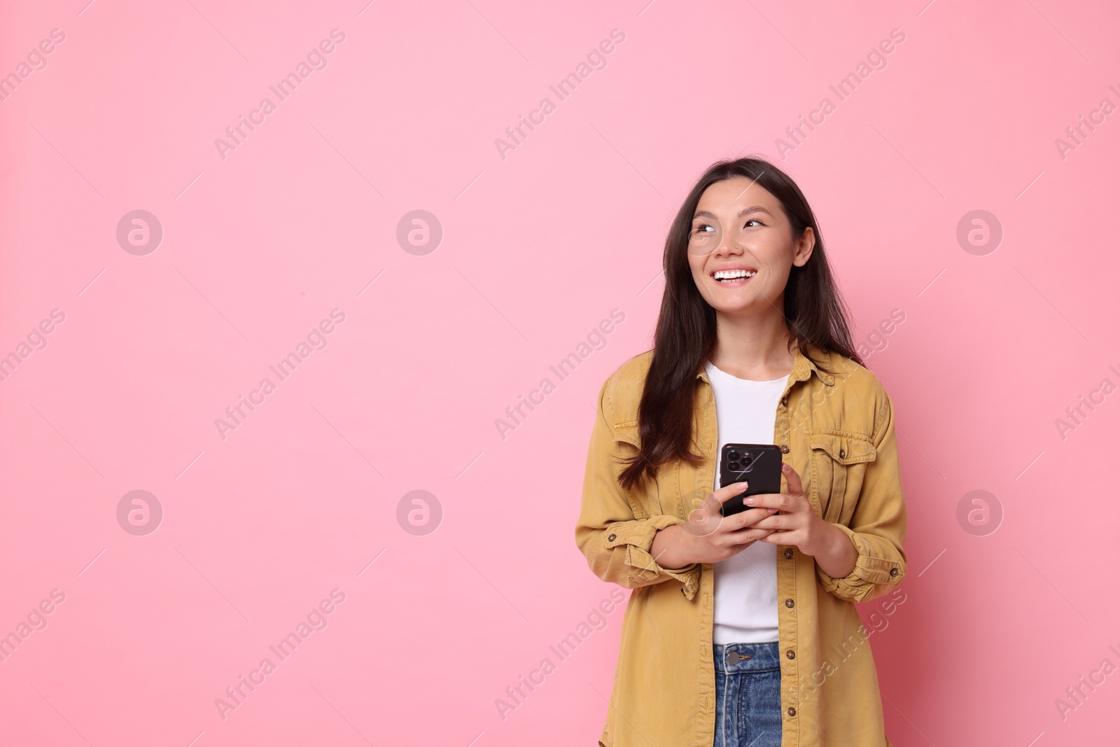 Photo of Smiling young woman with smartphone on pink background. Space for text