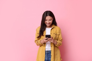 Photo of Smiling woman using smartphone on pink background