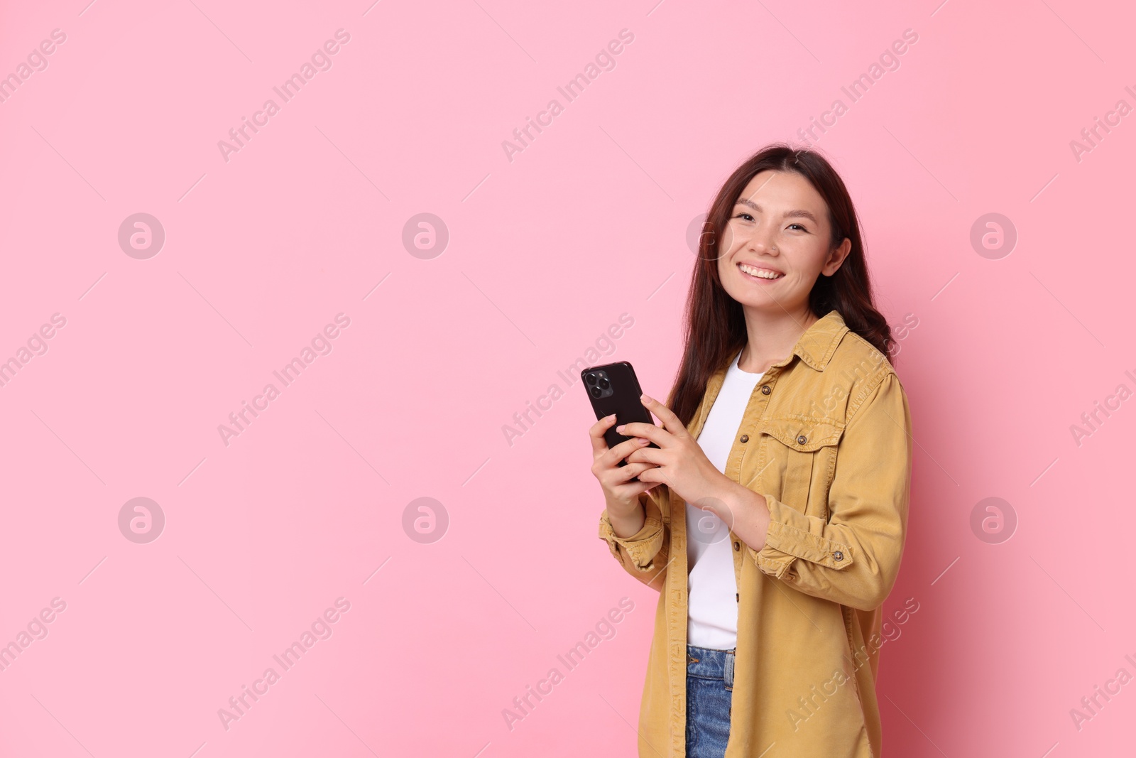 Photo of Smiling young woman with smartphone on pink background. Space for text