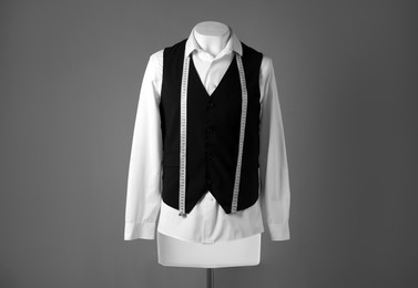 Male mannequin with black vest, white shirt and measuring tape on grey background