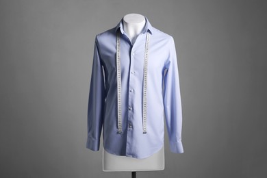 Male mannequin with light blue shirt and measuring tape on grey background