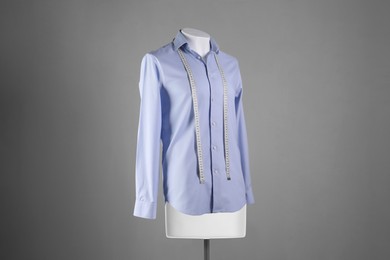 Male mannequin with light blue shirt and measuring tape on grey background