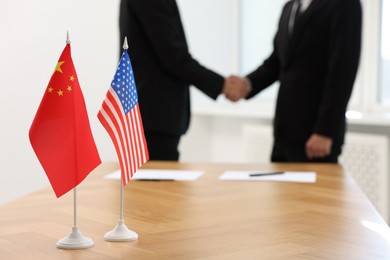 Diplomats shaking hands during meeting indoors, focus on flags of USA and China