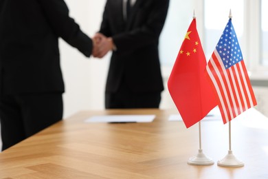 Diplomats shaking hands during meeting indoors, focus on flags of USA and China