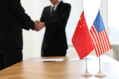 Diplomats shaking hands during meeting indoors, focus on flags of USA and China