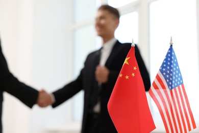 Diplomats shaking hands during meeting indoors, focus on flags of USA and China