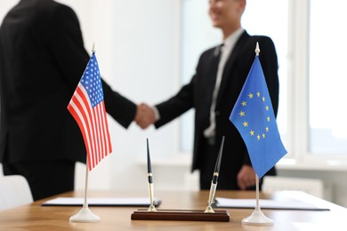 Photo of Diplomats shaking hands during meeting indoors, focus on flags of USA and European Union