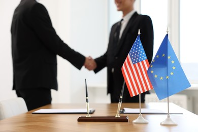 Diplomats shaking hands during meeting indoors, focus on flags of USA and European Union