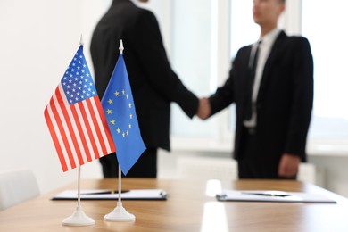 Diplomats shaking hands during meeting indoors, focus on flags of USA and European Union