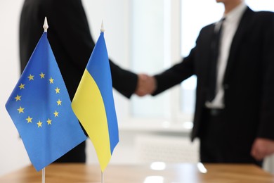 Diplomats shaking hands during meeting indoors, focus on flags of European Union and Ukraine