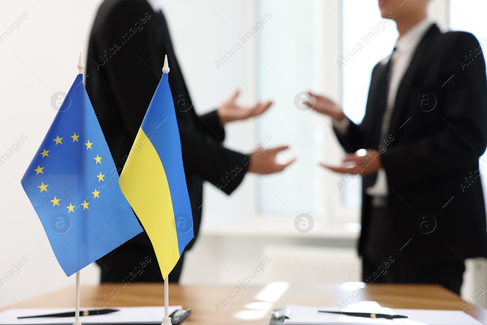 Photo of Diplomats negotiating during meeting indoors, focus on flags of European Union and Ukraine