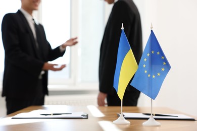 Diplomats negotiating during meeting indoors, focus on flags of European Union and Ukraine