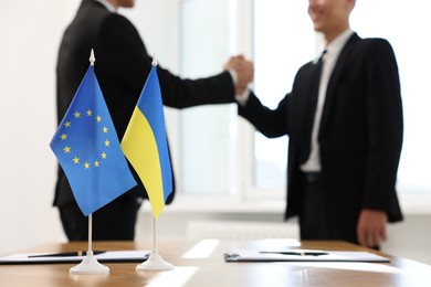 Diplomats shaking hands during meeting indoors, focus on flags of European Union and Ukraine