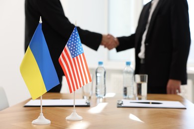 Photo of Diplomats shaking hands during meeting indoors, focus on flags of USA and Ukraine