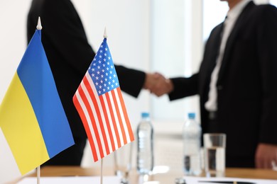 Diplomats shaking hands during meeting indoors, focus on flags of USA and Ukraine