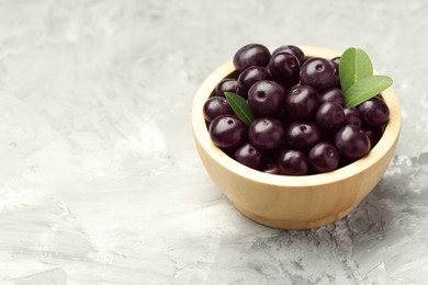 Photo of Ripe acai berries and leaves in bowl on grey textured table. Space for text