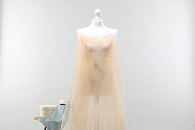 Photo of Mannequin with fabric and boxes on side table against light grey background. Creating new outfit