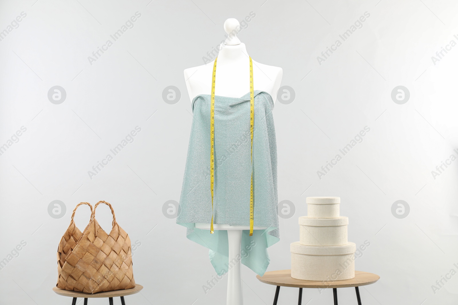 Photo of Mannequin with measuring tape, fabric, bag and boxes on side tables against light grey background. Creating new outfit