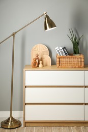 Photo of Different decorative elements on chest of drawers and lamp near gray wall indoors