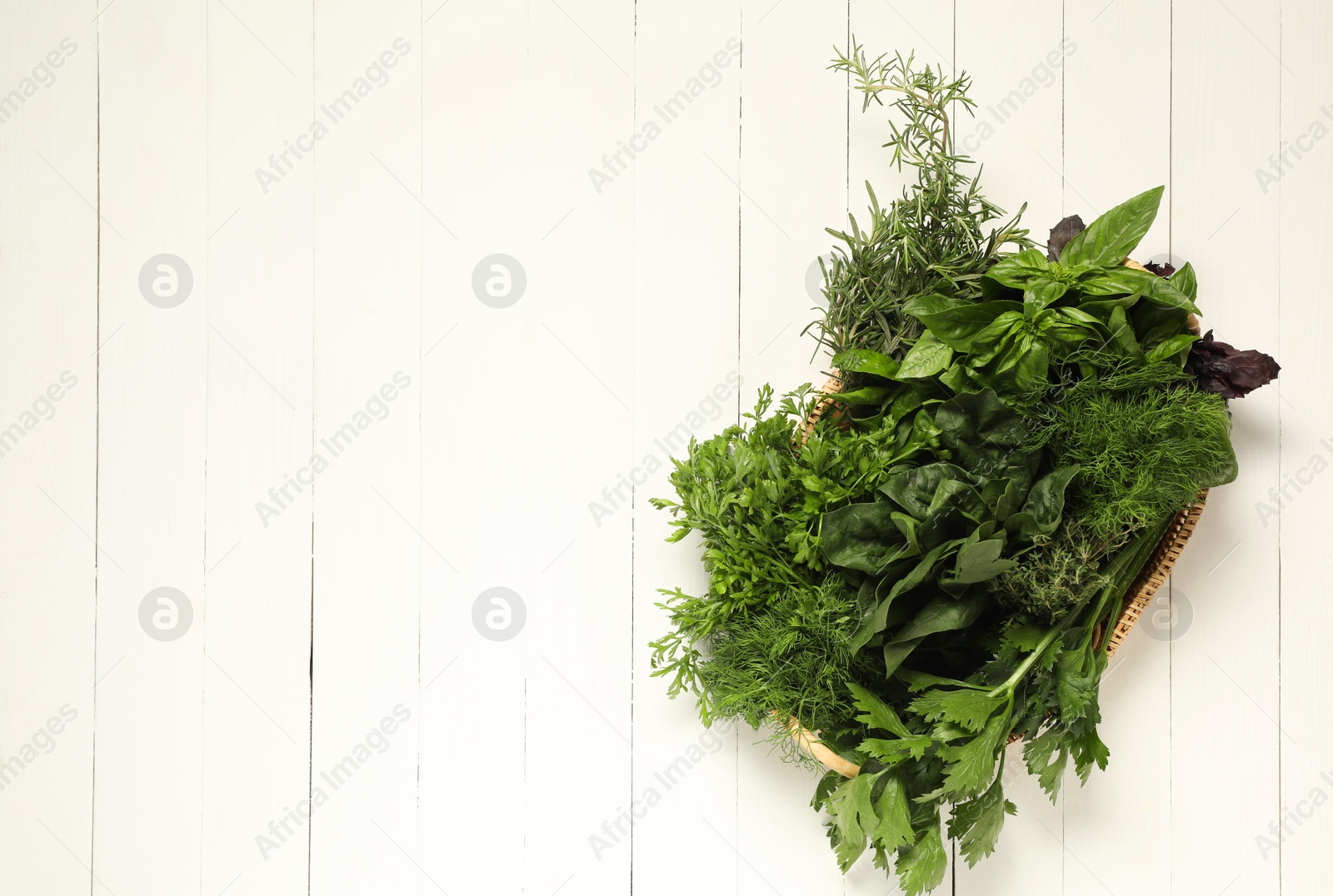 Photo of Different fresh herbs in basket on white wooden table, top view. Space for text