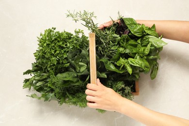 Photo of Woman holding different fresh herbs in wooden basket at light table, top view