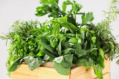 Photo of Different fresh herbs in wooden basket on light grey background, closeup