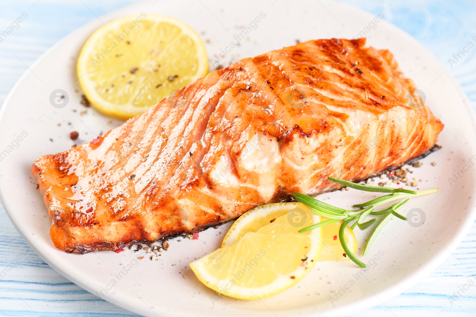 Photo of Delicious grilled salmon fillet served on light blue wooden table, closeup