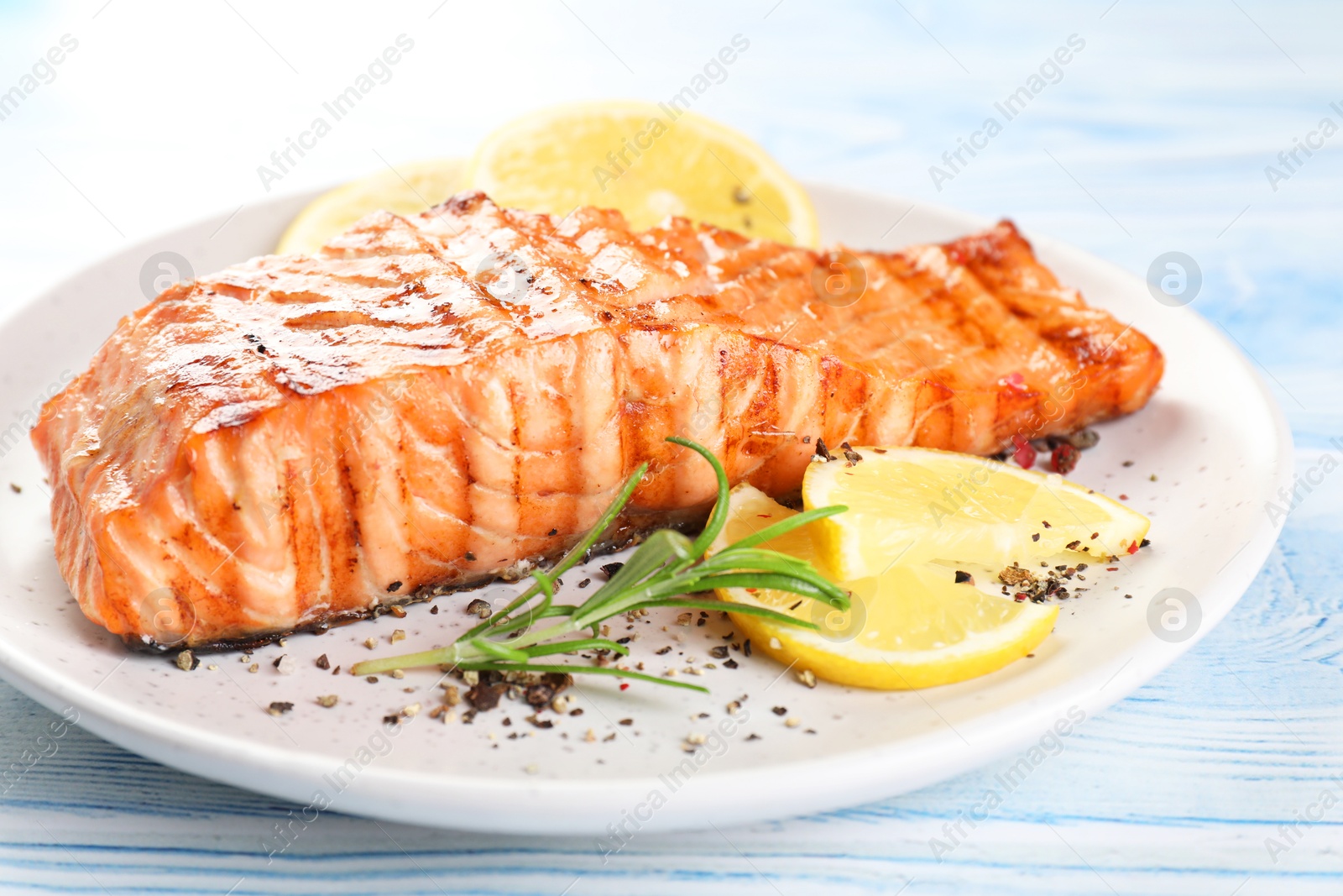 Photo of Delicious grilled salmon fillet served on light blue wooden table, closeup