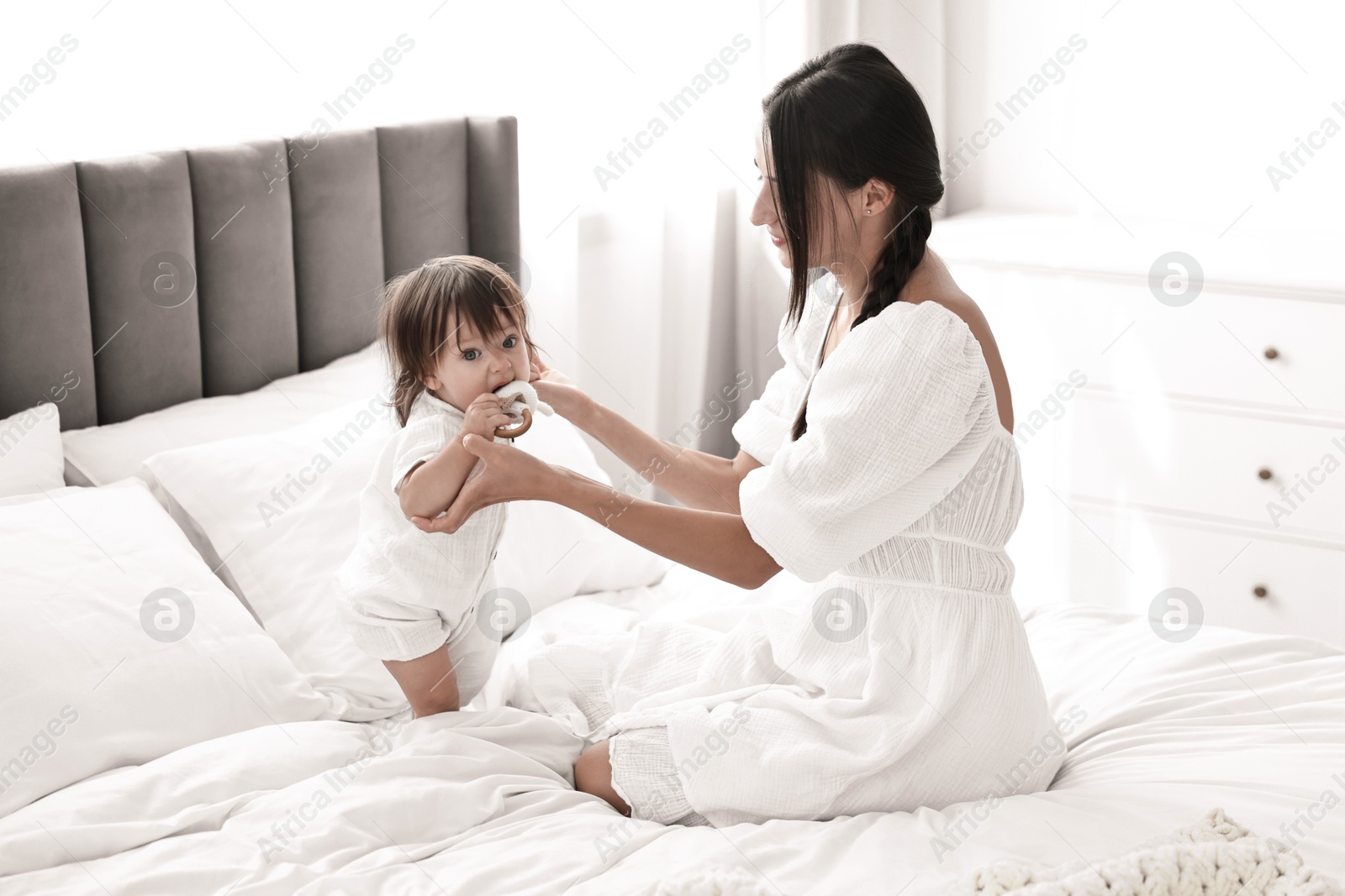 Photo of Beautiful young mother and her cute little baby with rattle on bed at home