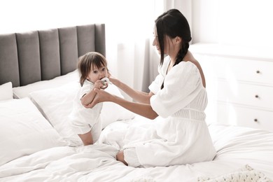 Photo of Beautiful young mother and her cute little baby with rattle on bed at home