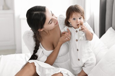 Beautiful young mother and her cute little baby with rattle on bed at home