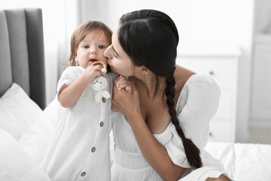 Photo of Beautiful young mother and her cute little baby with rattle on bed at home