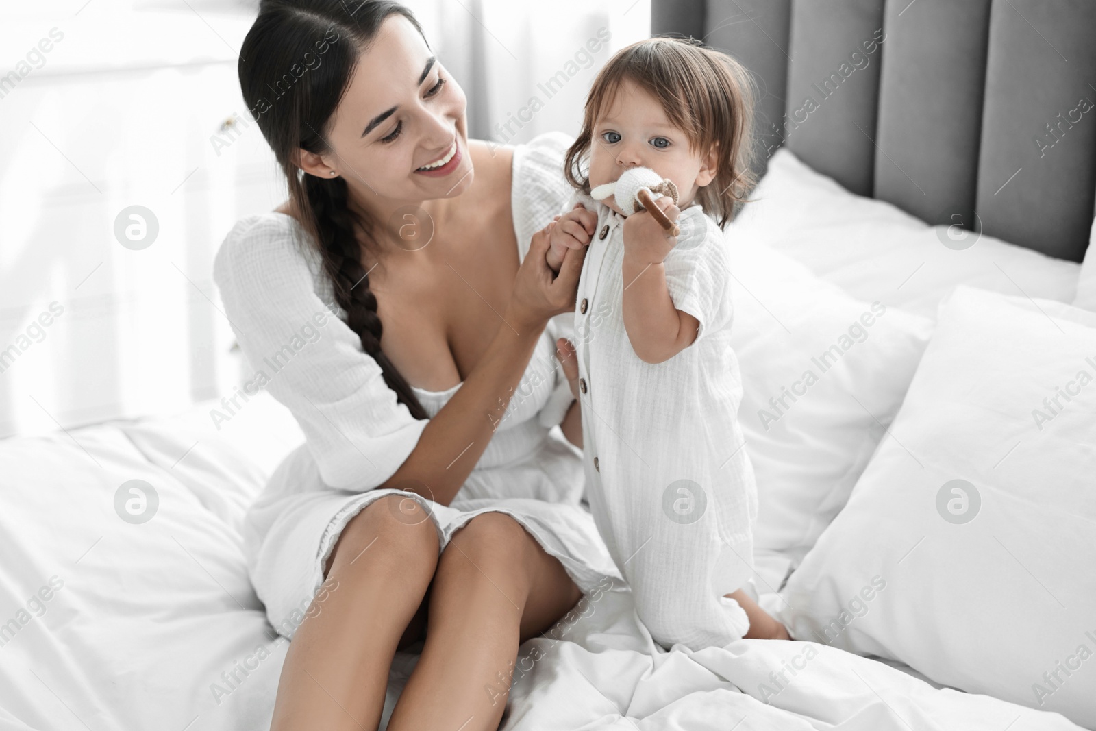 Photo of Beautiful young mother and her cute little baby with rattle on bed at home