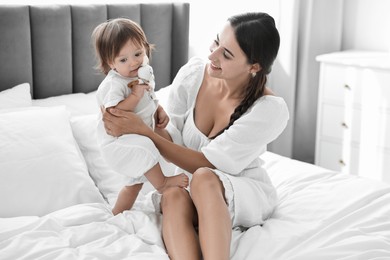 Beautiful young mother and her cute little baby with rattle on bed at home