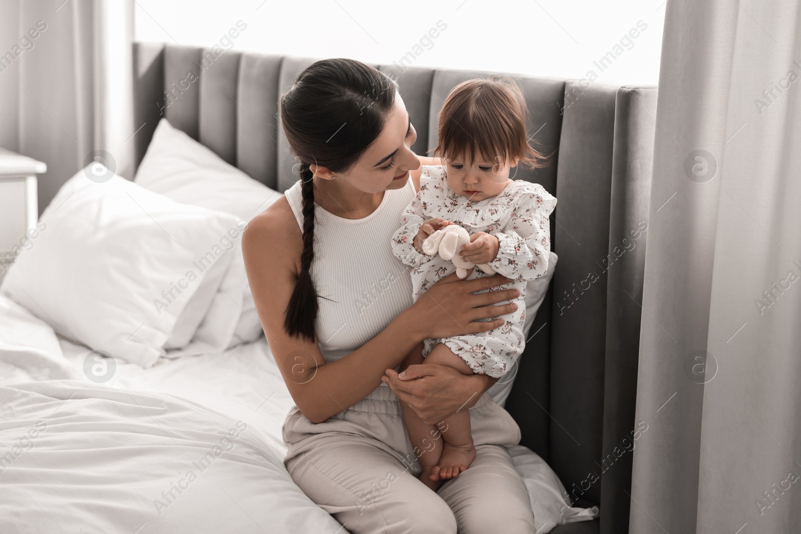 Photo of Beautiful young mother and her cute little baby with rabbit toy on bed at home