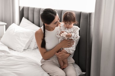 Beautiful young mother and her cute little baby with rabbit toy on bed at home