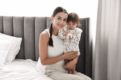 Photo of Beautiful young mother and her cute little baby with rabbit toy on bed at home