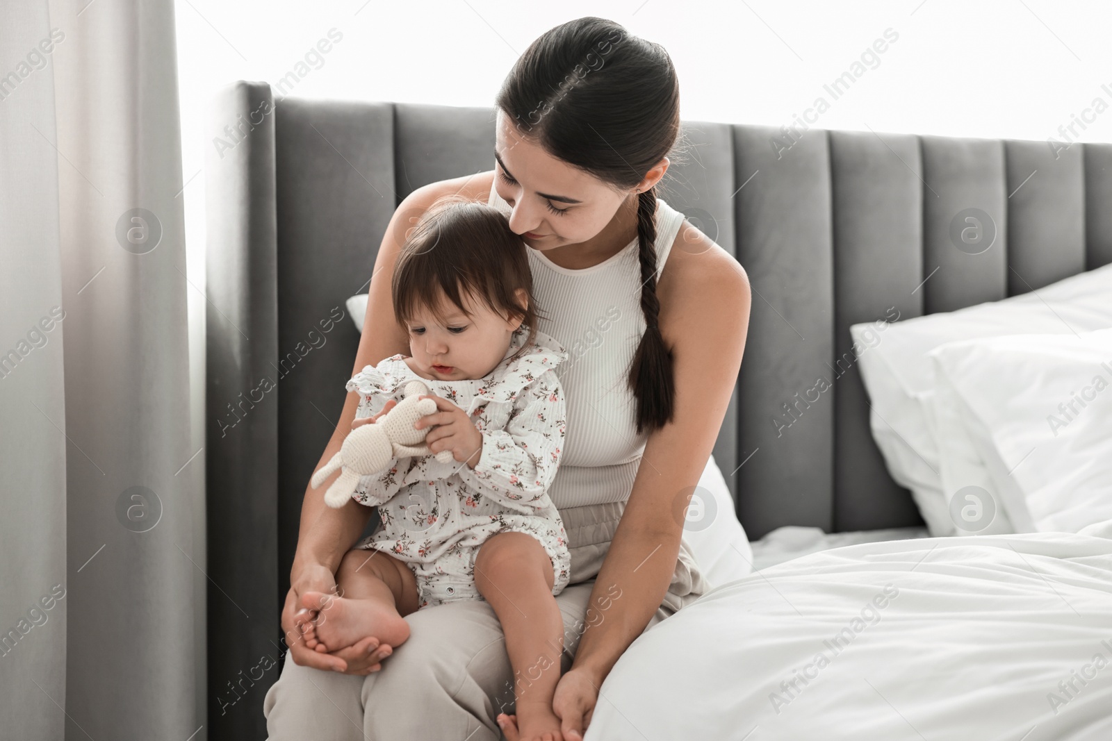 Photo of Beautiful young mother and her cute little baby with rabbit toy on bed at home