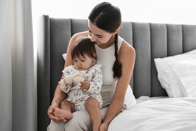 Photo of Beautiful young mother and her cute little baby with rabbit toy on bed at home