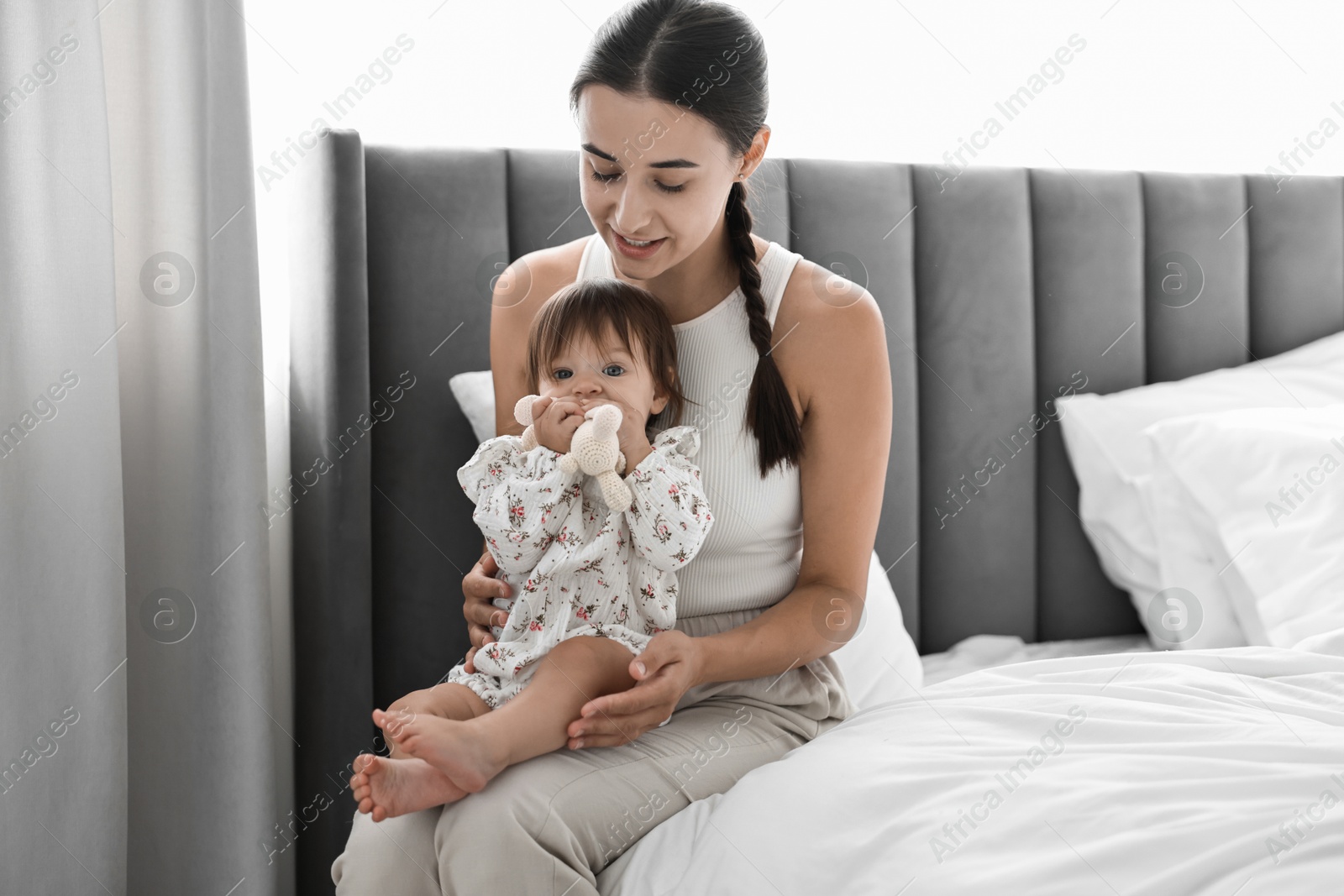 Photo of Beautiful young mother and her cute little baby with rabbit toy on bed at home