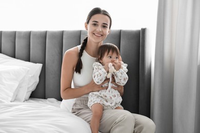 Photo of Beautiful young mother and her cute little baby with rabbit toy on bed at home