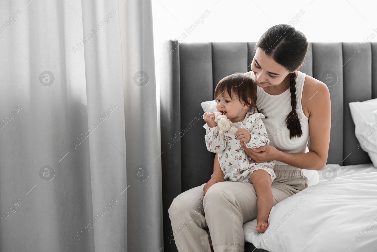 Photo of Beautiful young mother and her cute little baby with rabbit toy on bed at home, space for text